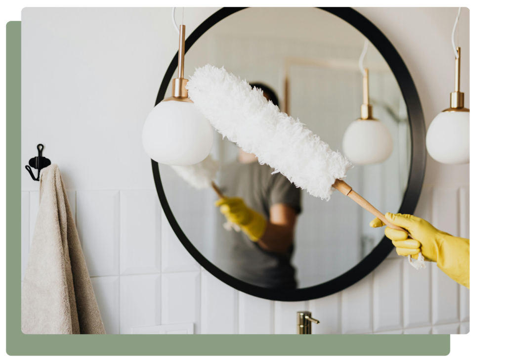 Cleaner dusting a bathroom mirror during standard house cleaning